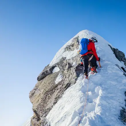 Homem escalando o cume de uma montanha com neve